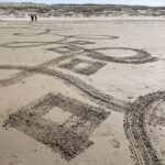 vormtekening gemaakt met hark op strand met in de verte Nymphaea